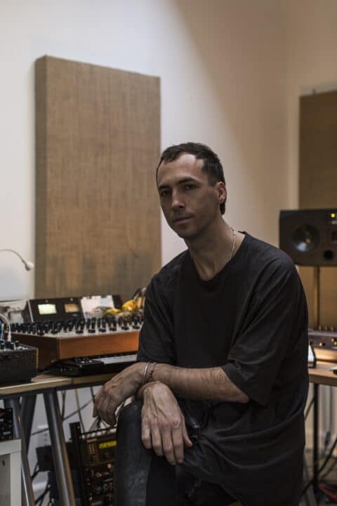 Tim Hecker poses in front of music equipment